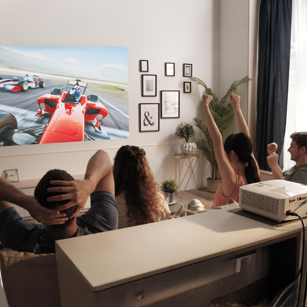 Group of friends cheering while watching a high-speed racing event on a regular throw projector in a cozy living room — immersive large-screen entertainment for home cinema setups